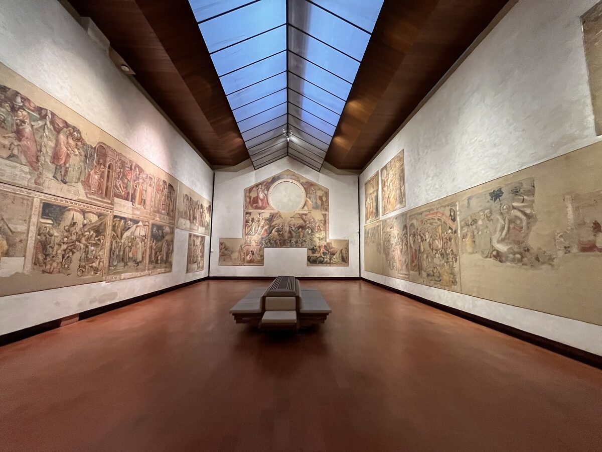 The hall of medieval frescoes in the Pinacoteca Nazionale under a glass roof, with a bench in the middle