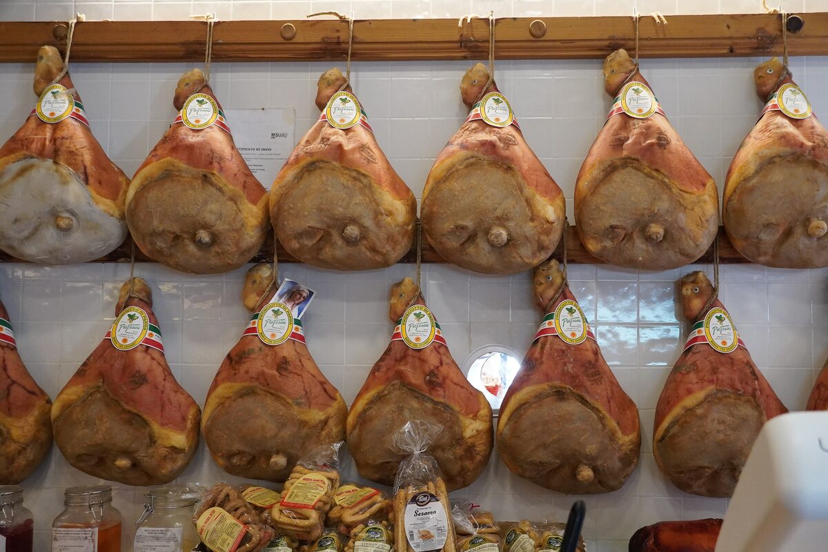 Rows of Prosciutto di Parma hams with their crown stamps hanging on a white-tiled deli wall