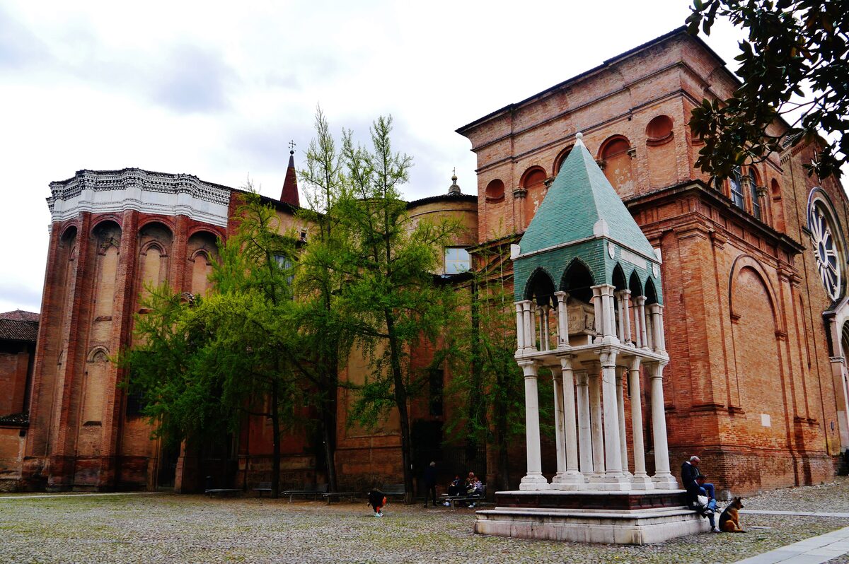 A green-roofed canopy tomb on a stone base, beside the brick walls of San Domenico