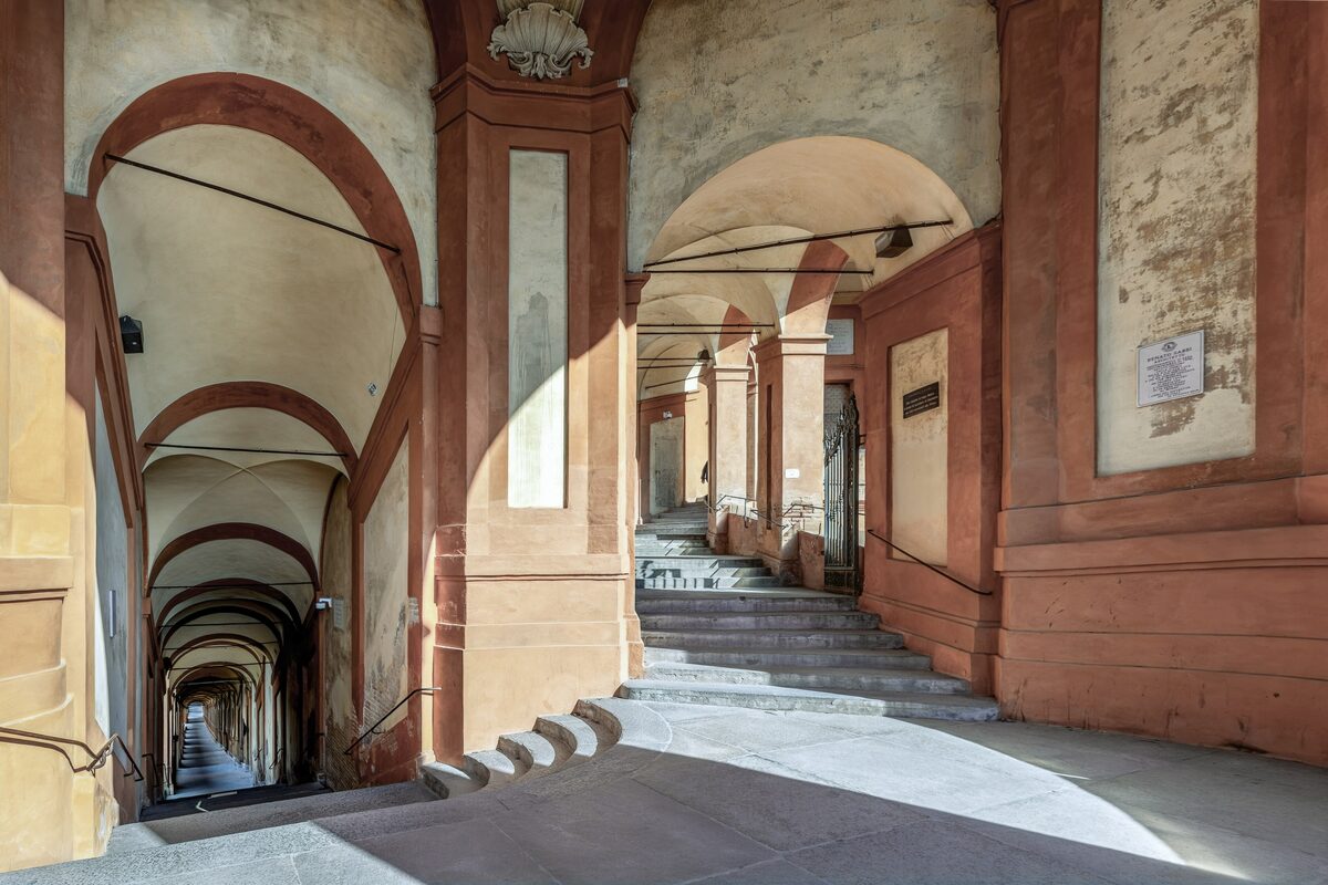 The arched portico of San Luca climbing a staircase between pink walls in strong sunlight