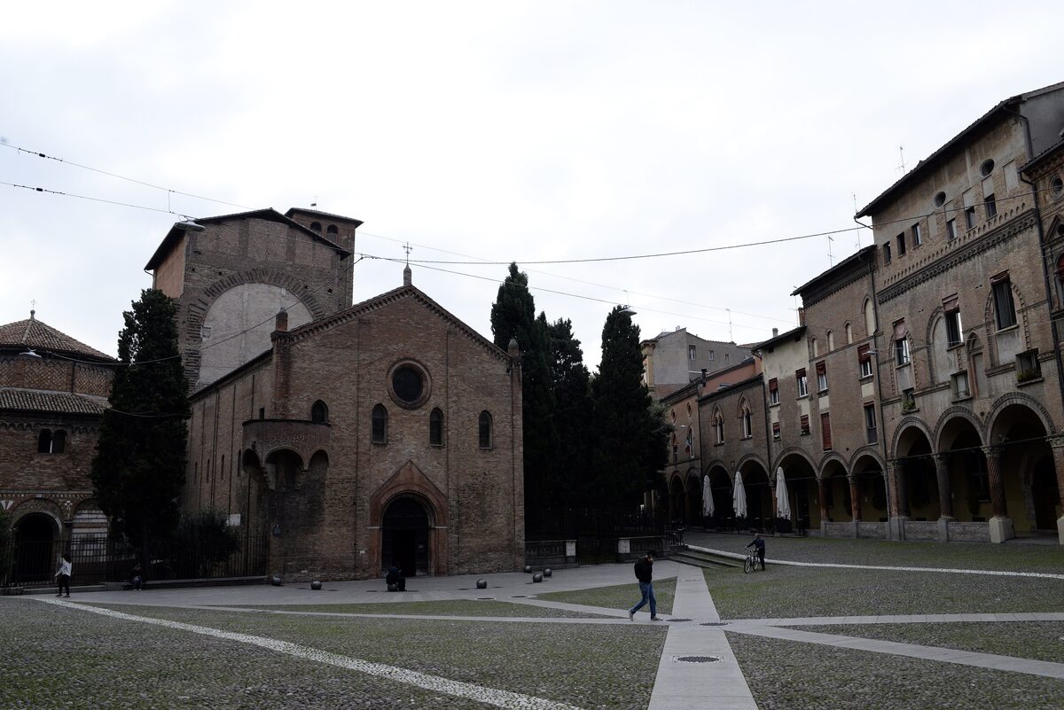Piazza Santo Stefano with its brick church under a pale sky, arcaded houses on the right