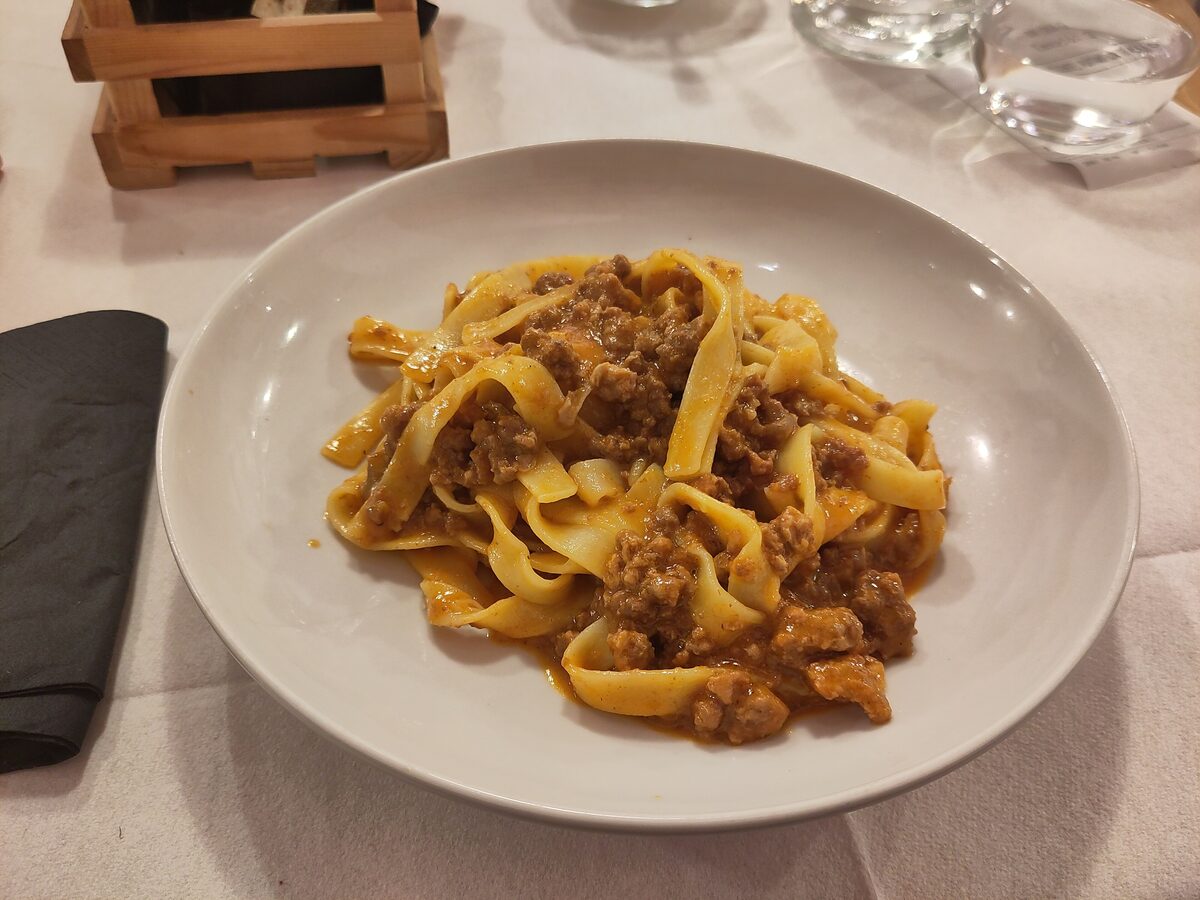 Flat egg tagliatelle tossed with a brown meat ragù on a white plate