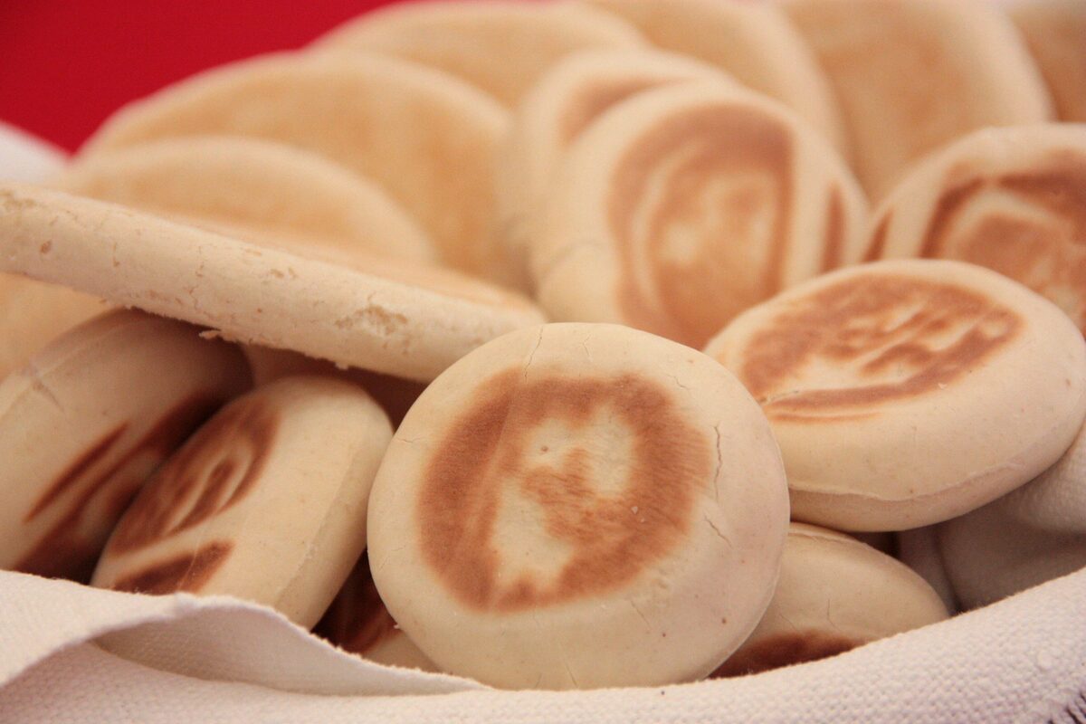 Round tigelle flatbreads, golden and puffed, piled in a basket