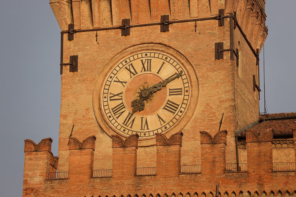 The brick clock tower of Palazzo d'Accursio, its Roman-numeral clock face under the battlements