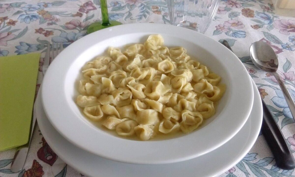 Small tortellini floating in clear broth in a white bowl