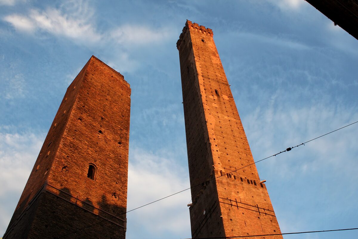 The two brick towers seen from below against a blue sky, the shorter one leaning