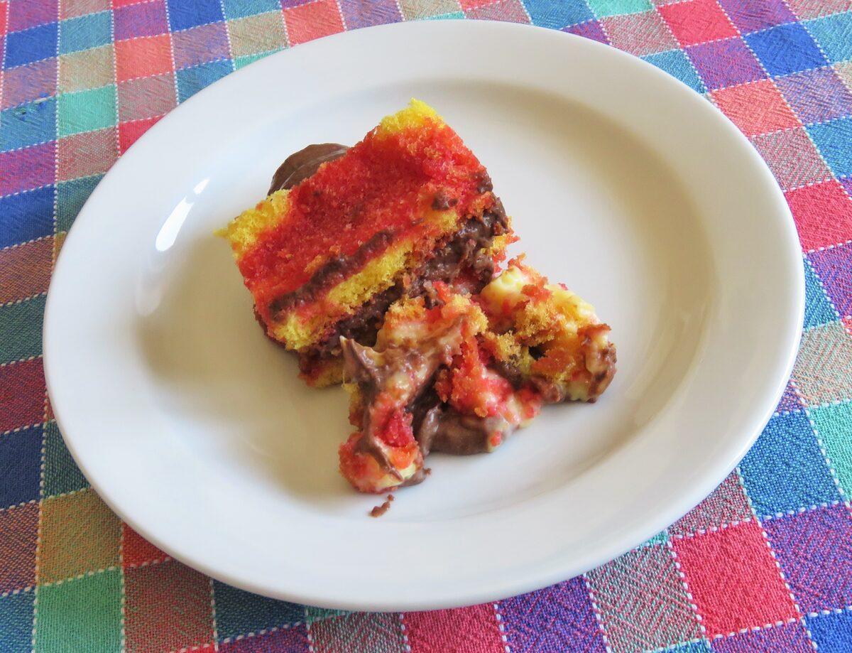 A slice of zuppa inglese on a plate, red alchermes-soaked and yellow sponge layered with chocolate and custard