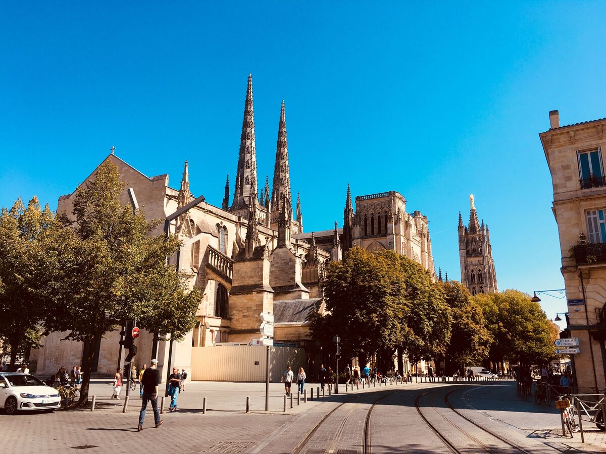 The twin Gothic spires of the Cathédrale Saint-André in Bordeaux above trees, with the separate Pey-Berland bell tower on the right