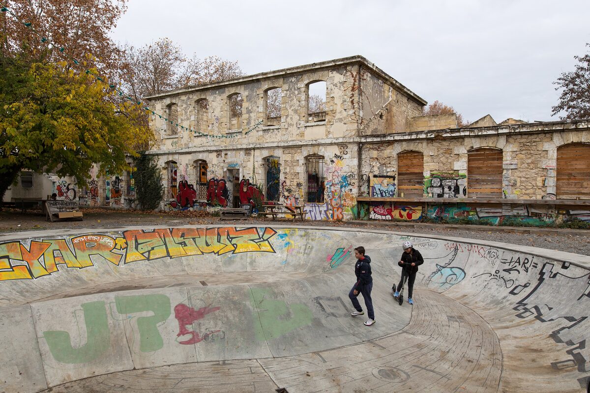 Skateboarders in a graffiti-covered concrete bowl in front of an old stone barracks building at Darwin