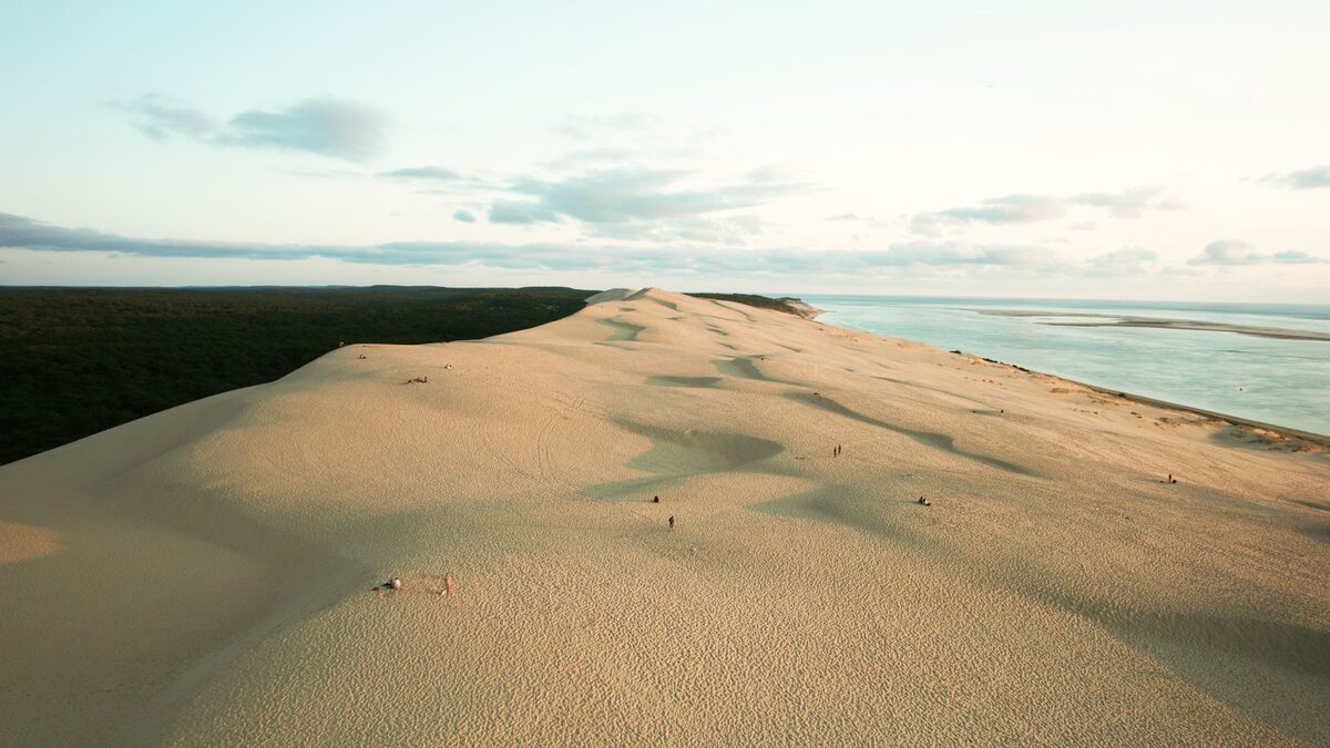 Aerial view of the huge pale Dune du Pilat between the dark pine forest and the ocean, under scattered clouds