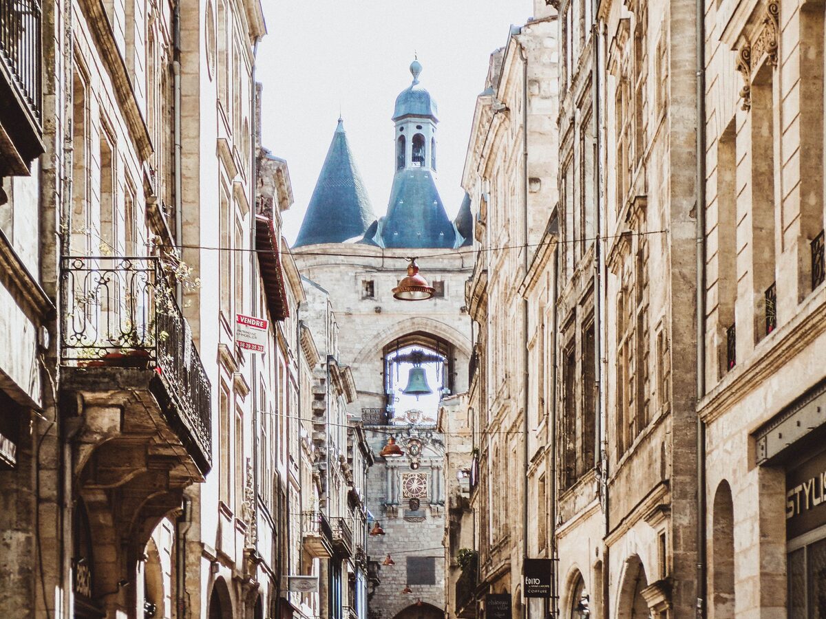 The Grosse Cloche, a stone gate with two pointed towers and a bell hanging in its arch, at the end of a narrow street of old stone buildings