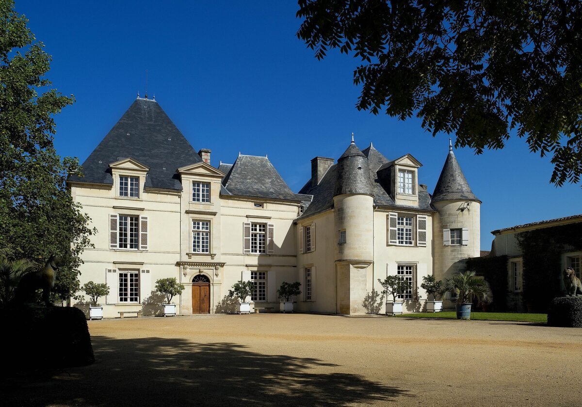 The white stone château of Haut-Brion with slate roofs and round towers, seen across a sunny gravel courtyard