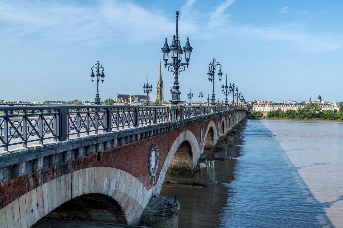 The red brick and stone arches of the Pont de Pierre over the wide Garonne, with ornate lampposts along the bridge