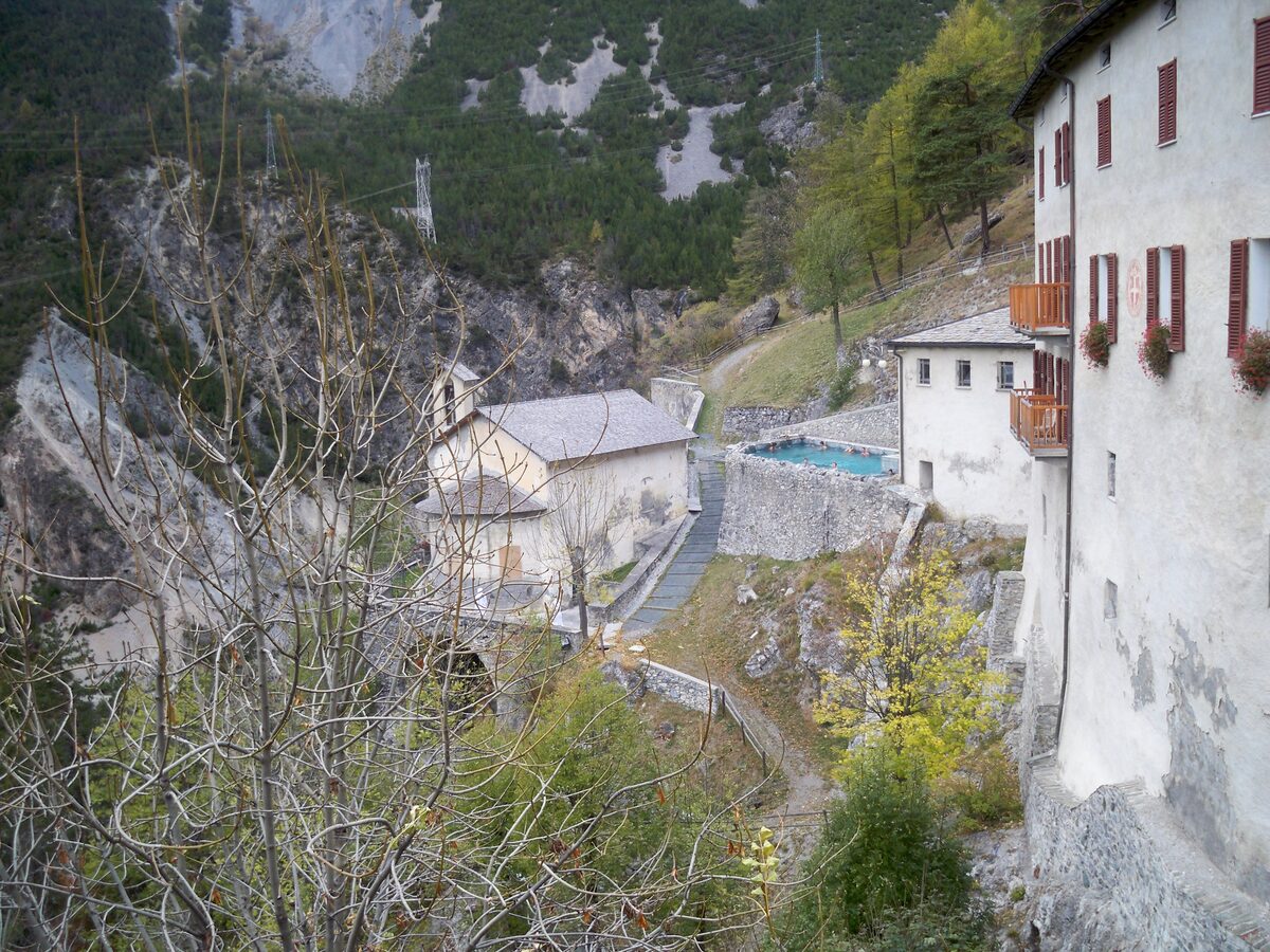 The outdoor pool of the Bagni Vecchi thermal baths, set into the rock below a white stone building in the valley