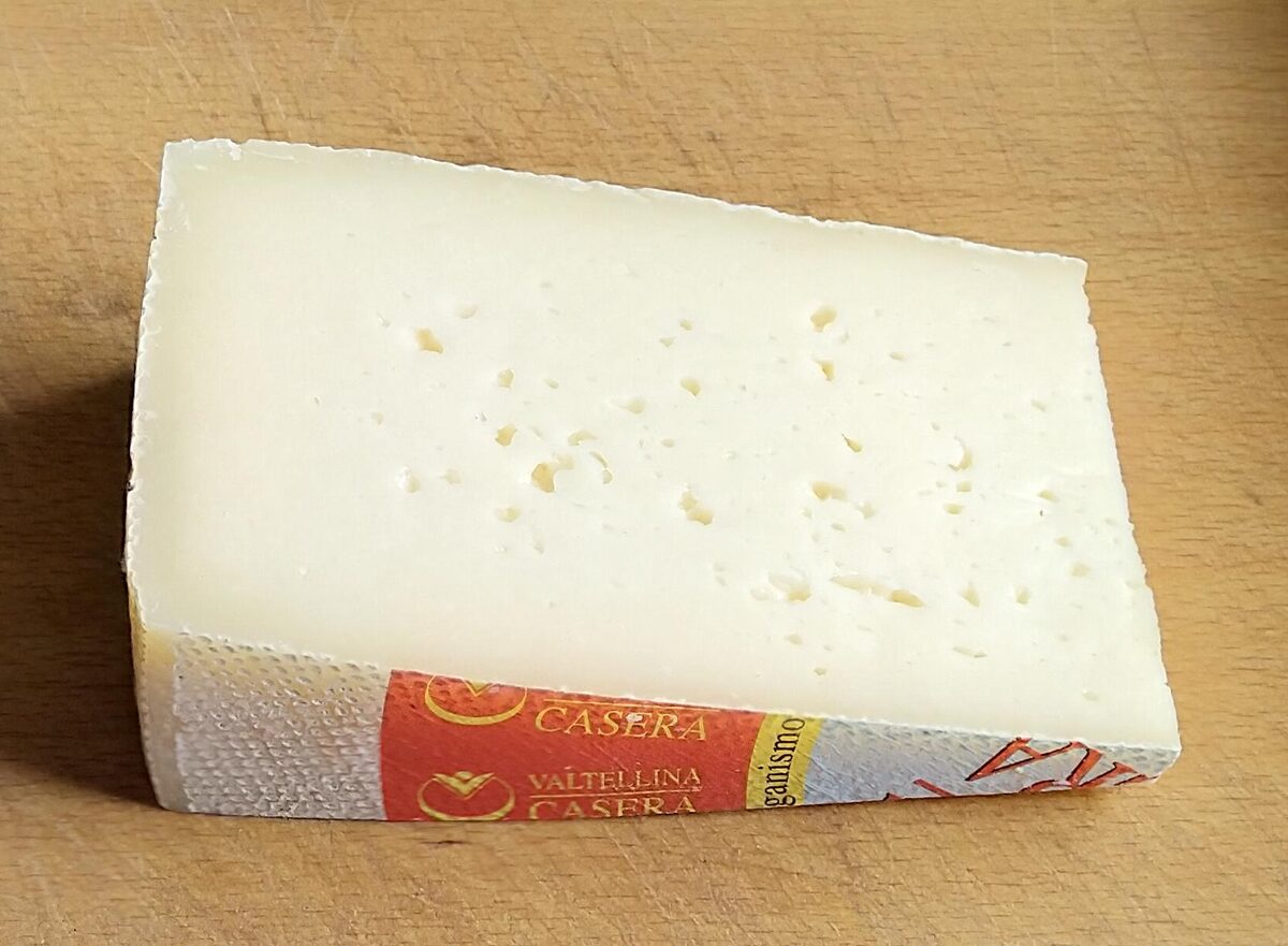 A wedge of Valtellina Casera cheese with its red and gold label on a wooden board
