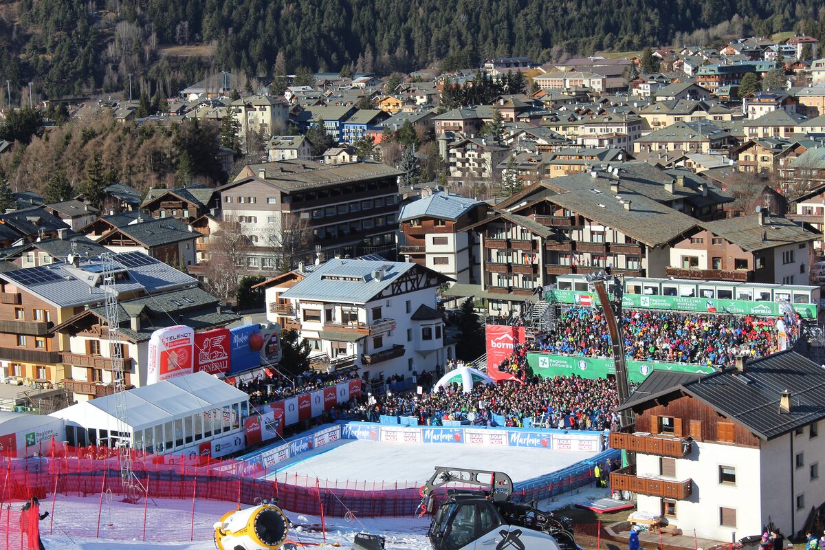 The finish area of the Stelvio piste in Bormio, with a crowd behind the red barriers and the town rising behind