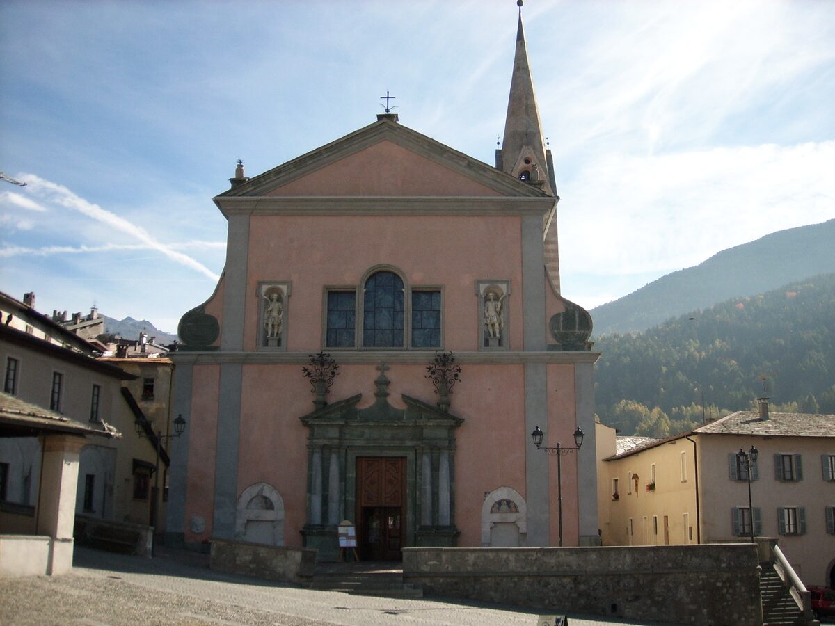 The pink facade of the Collegiata of Santi Gervasio e Protasio in Bormio, with its tall spire