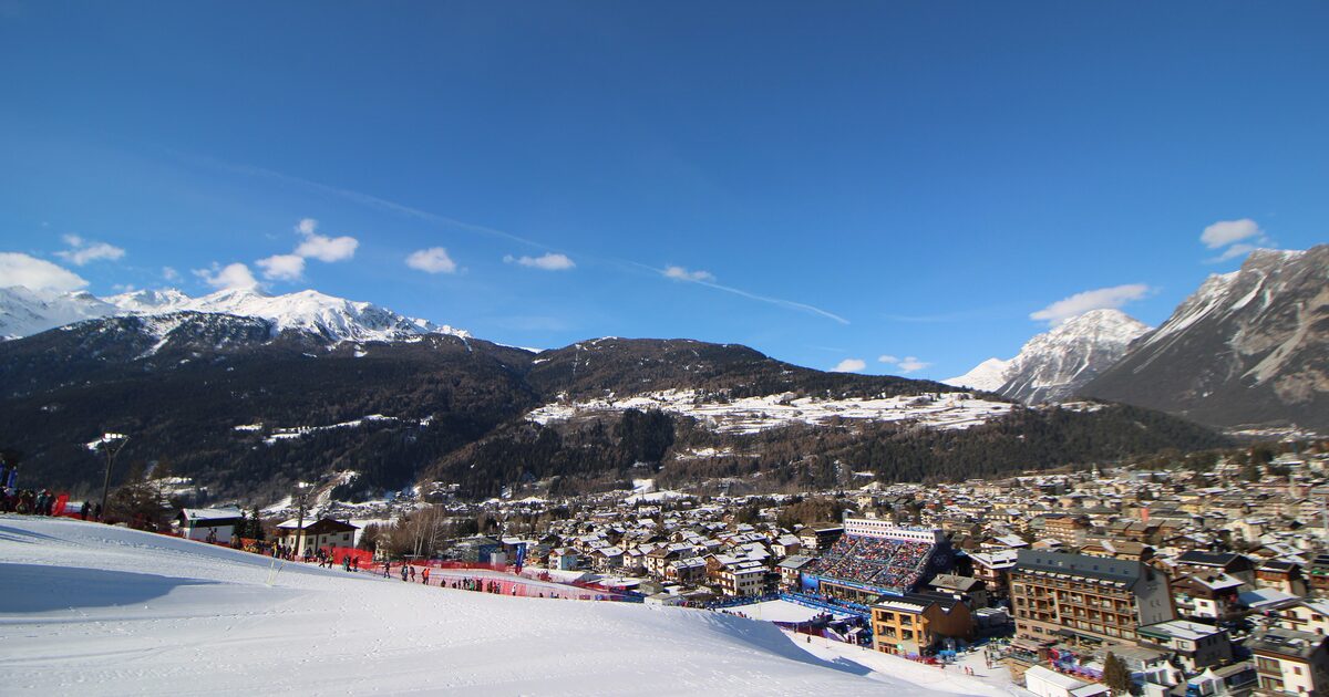 Bormio under fresh snow on a bright February day, seen from the Stelvio piste, with the Olympic finish stadium and the town below the mountains
