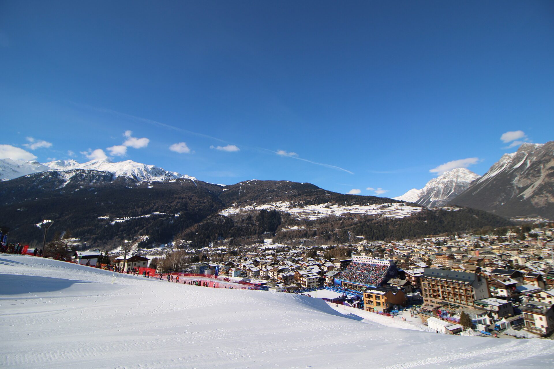 Bormio under fresh snow on a bright February day, seen from the Stelvio piste, with the Olympic finish stadium and the town below the mountains