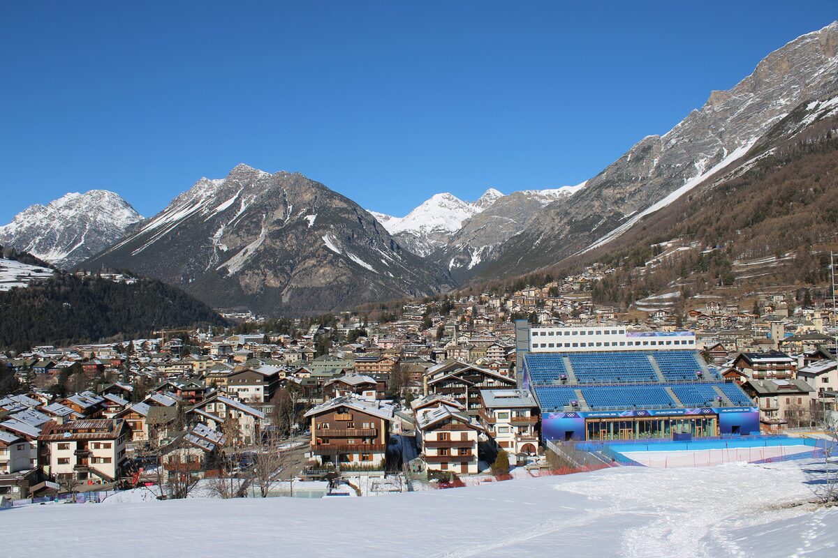 The blue Olympic grandstand of the Stelvio Ski Centre in Bormio, with the town roofs and snowy mountains around it