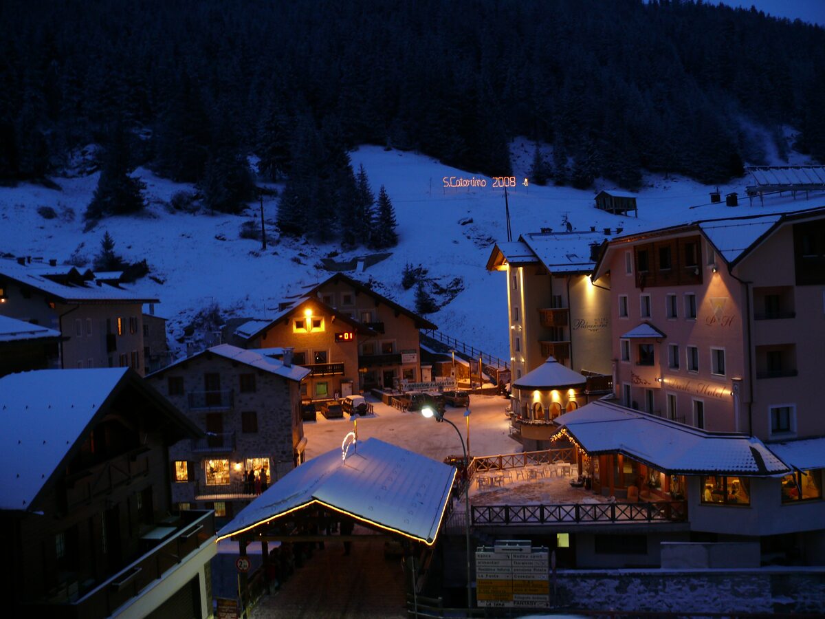 The village of Santa Caterina Valfurva at dusk after fresh snow, with snow on the roofs, lit hotel windows and a lit sign on the slope behind