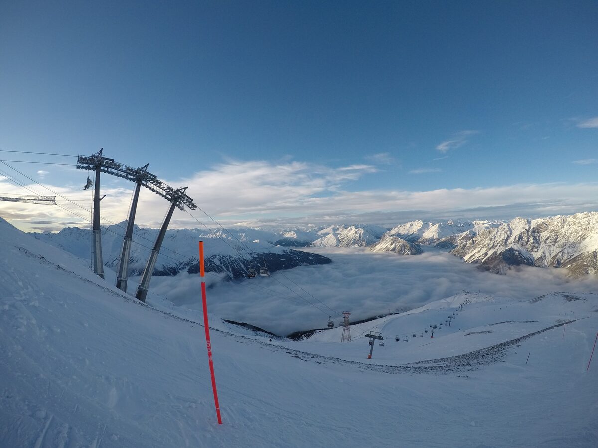 Chairlift pylons on a snowy ridge near Bormio 3000, with a sea of cloud filling the valley below and white peaks beyond