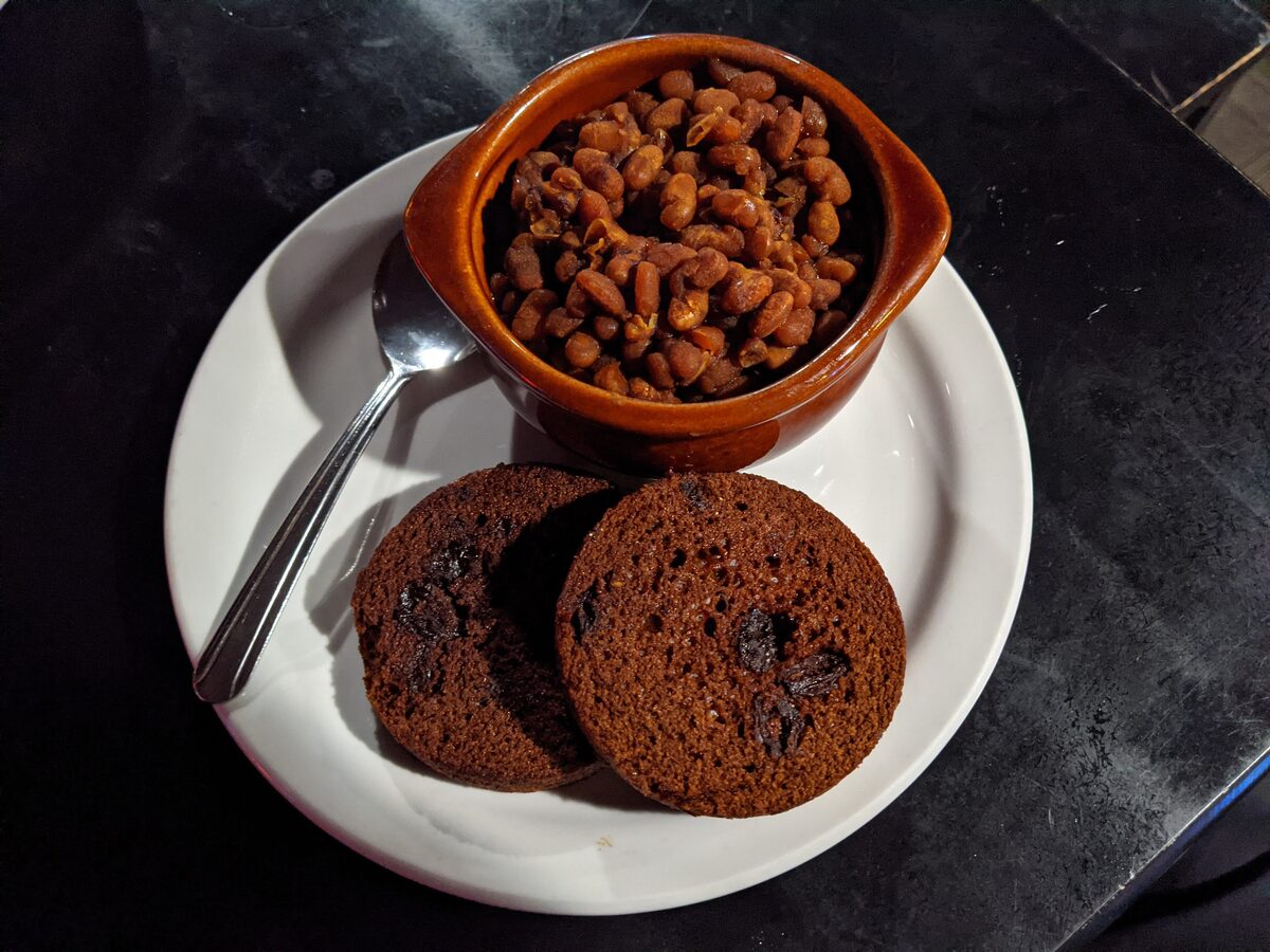 A crock of baked beans beside two slices of brown bread