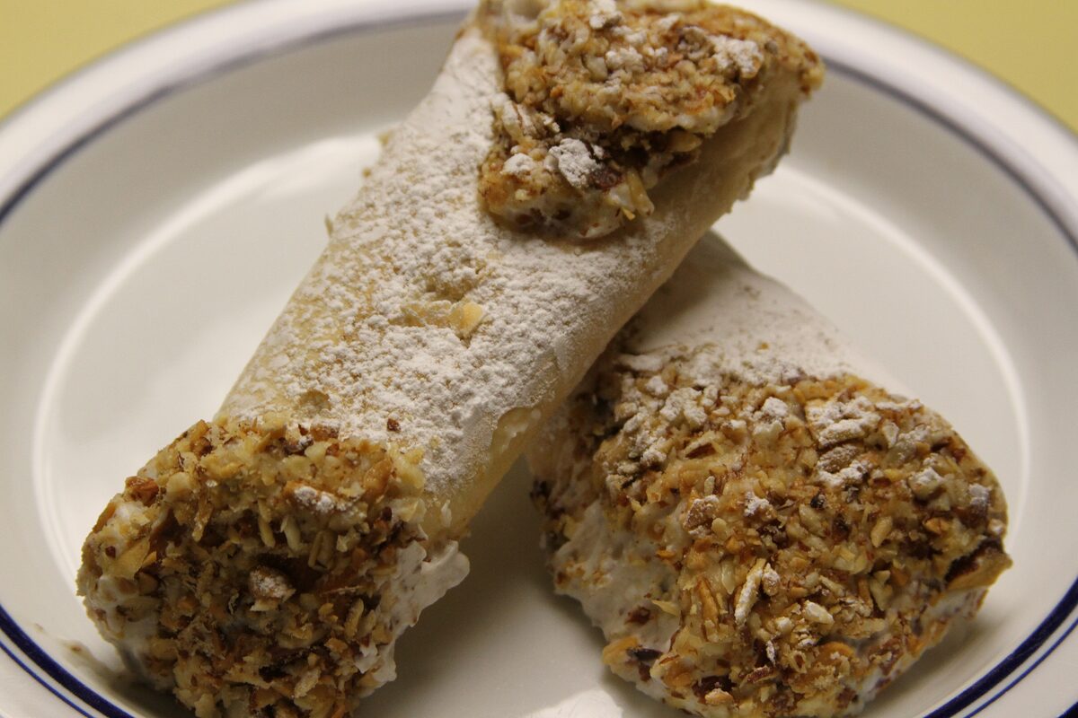 Two ricotta cannoli rolled in chopped pistachios and dusted with sugar