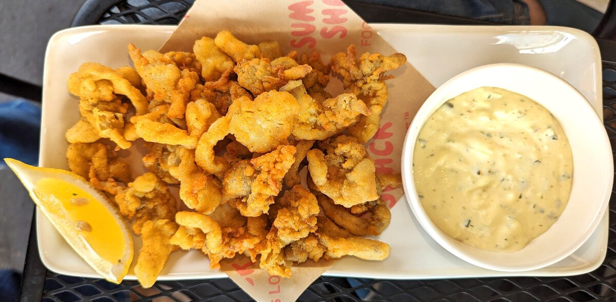 A plate of golden fried whole-belly clams with tartar sauce and lemon