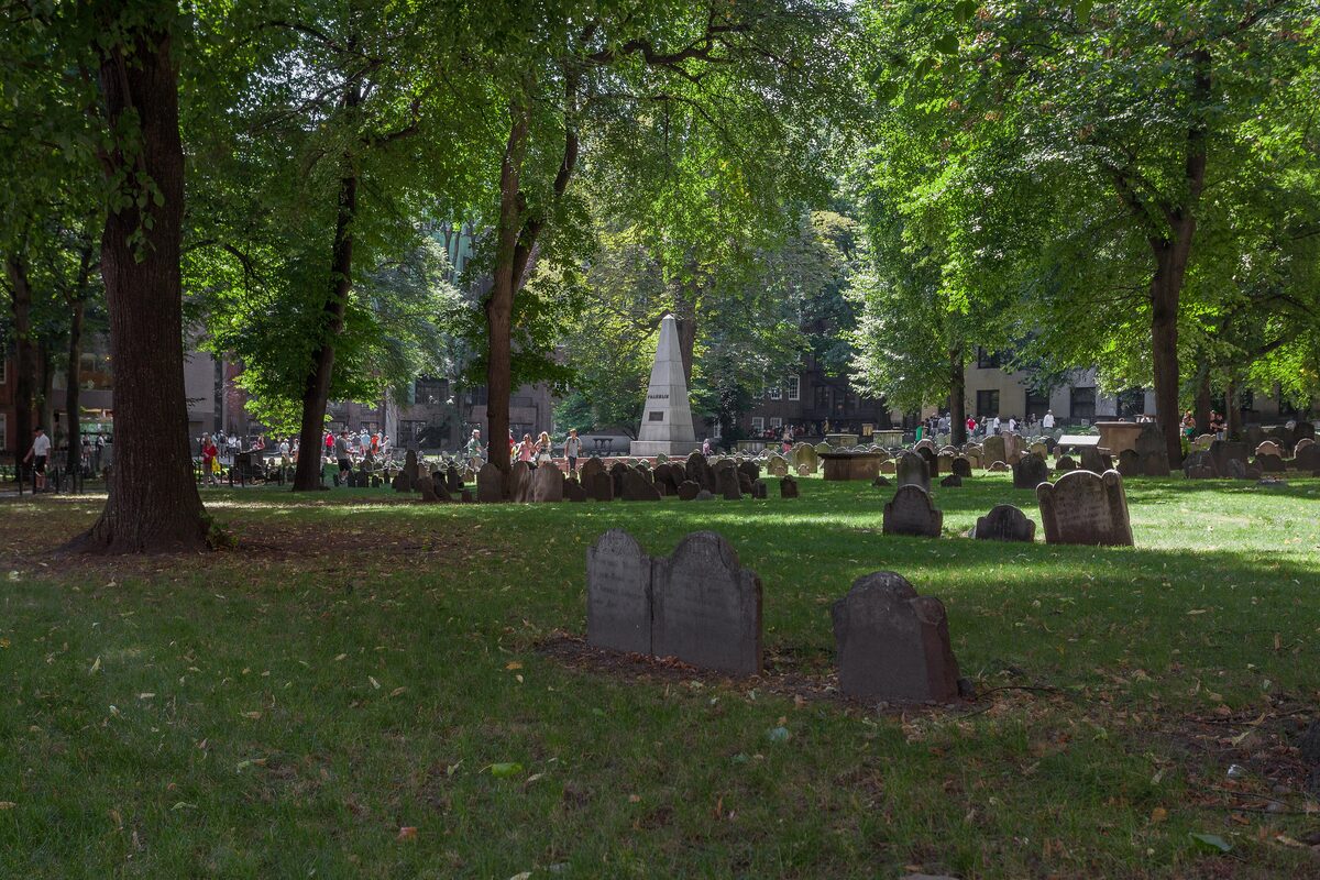 Old slate gravestones under shade trees with the Franklin obelisk beyond