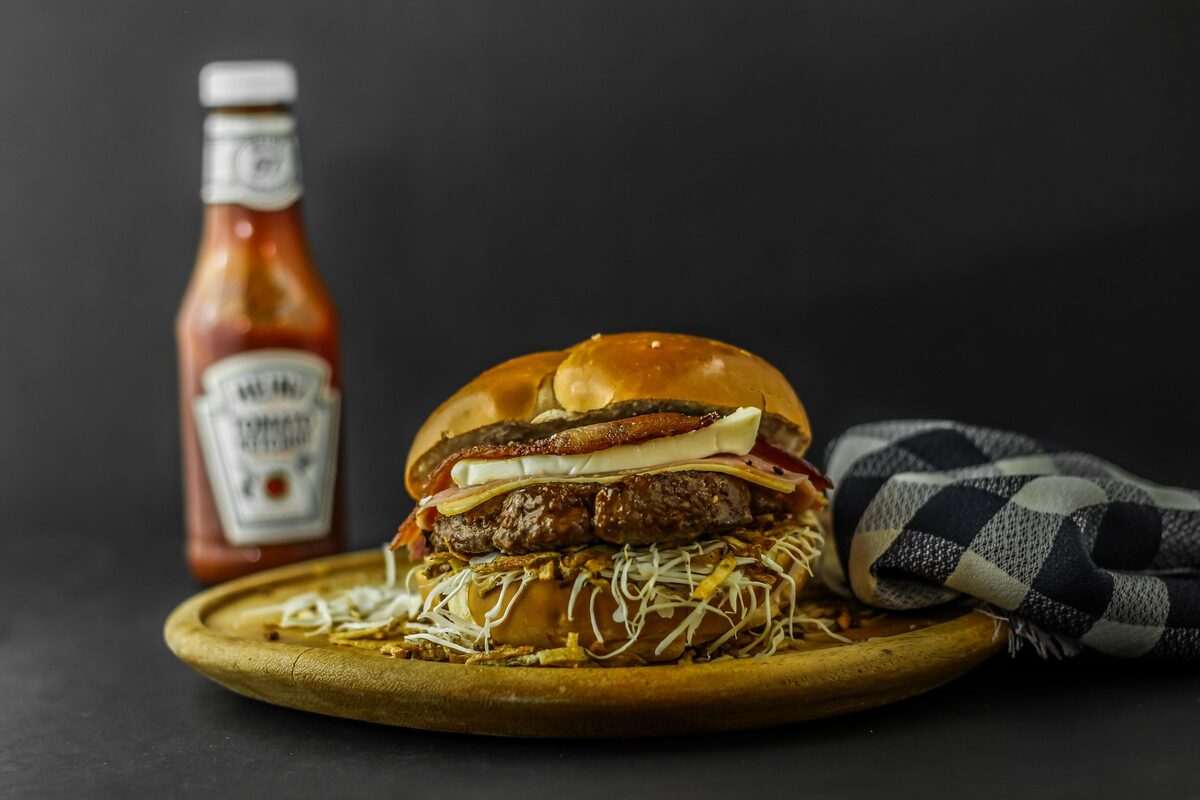A cheeseburger on a wooden board beside a ketchup bottle