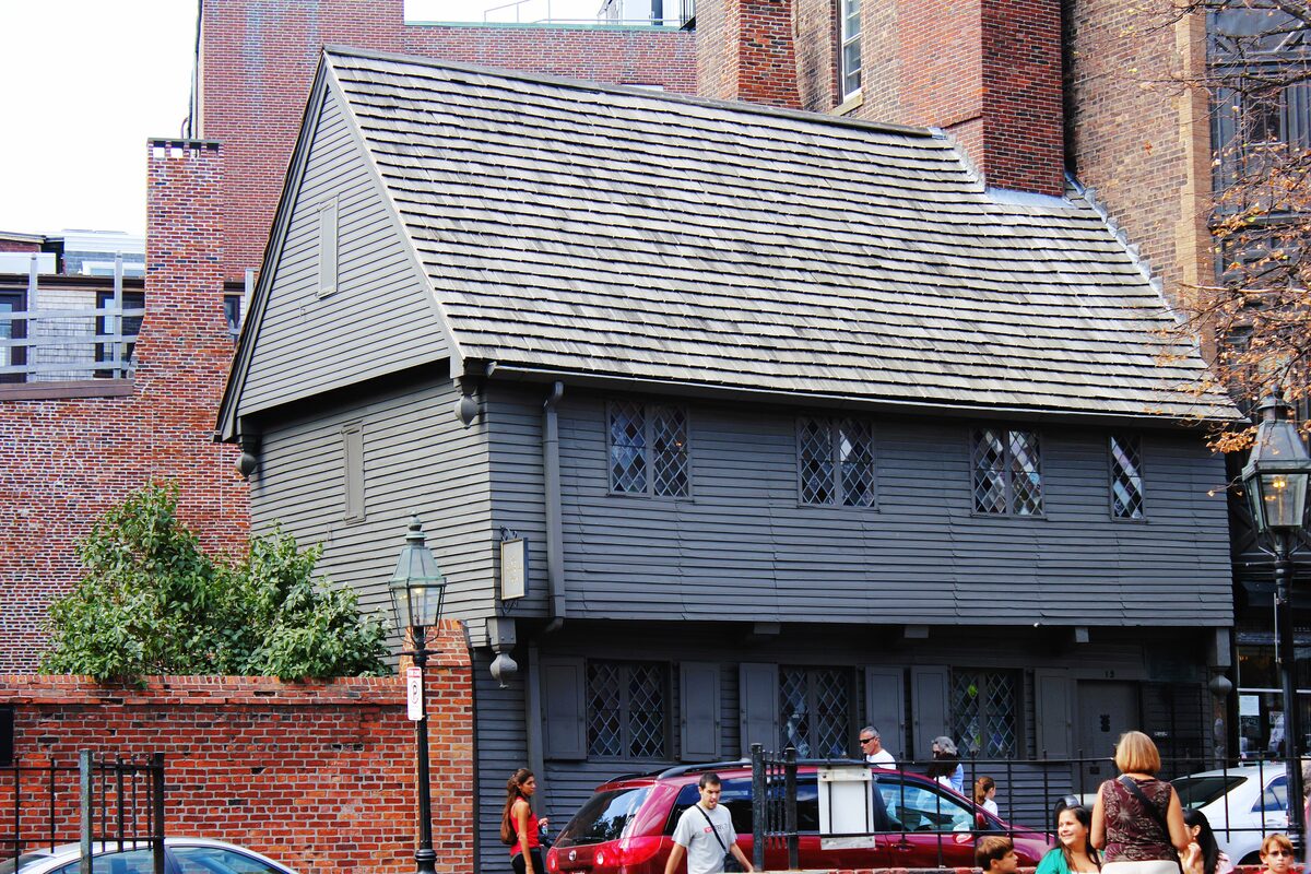 The small gray-timbered Paul Revere House beside a brick wall