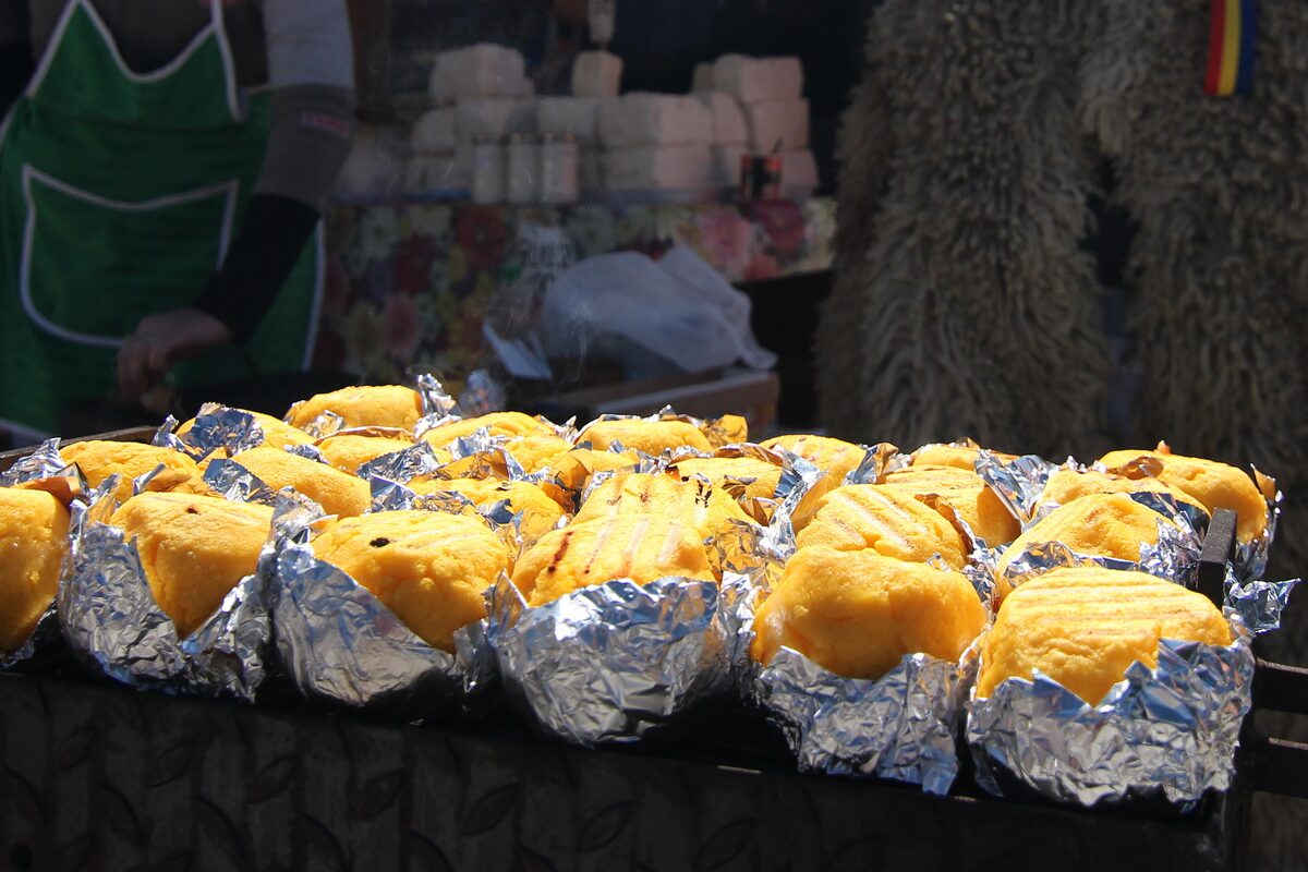 Rows of golden baked bulz, polenta balls stuffed with cheese, wrapped in foil on a market stall