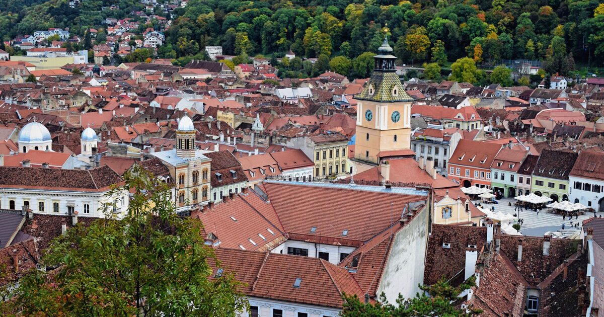 The red roofs of Brașov's old town from above, with the Council House tower in the middle and the wooded slope of Tâmpa behind