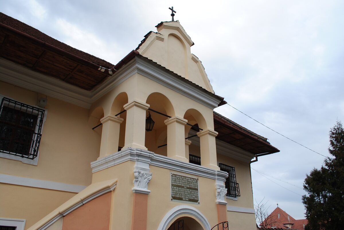 The cream and pink facade of the First Romanian School in Brașov, with an arched porch and steps