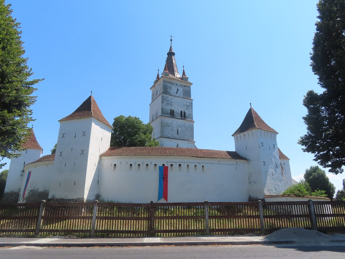 The fortified church at Hărman, with white walls, squat towers with red roofs and a tall bell tower in the middle
