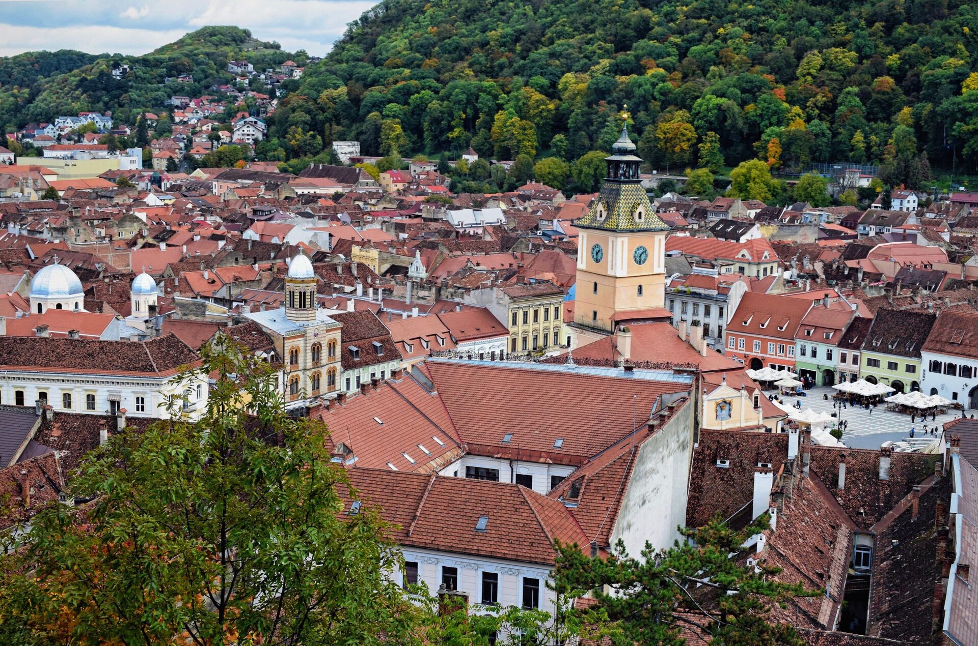 The red roofs of Brașov's old town from above, with the Council House tower in the middle and the wooded slope of Tâmpa behind