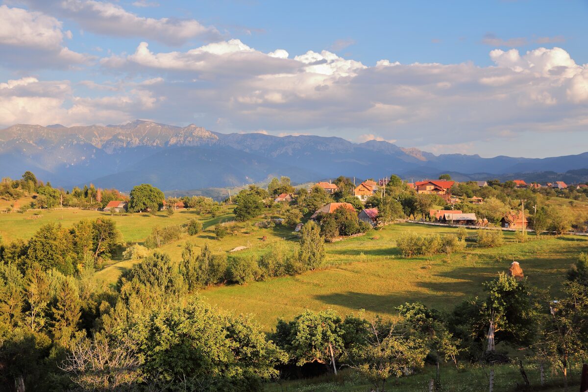 Green meadows and scattered houses of Măgura village, with the long rocky ridge of Piatra Craiului behind