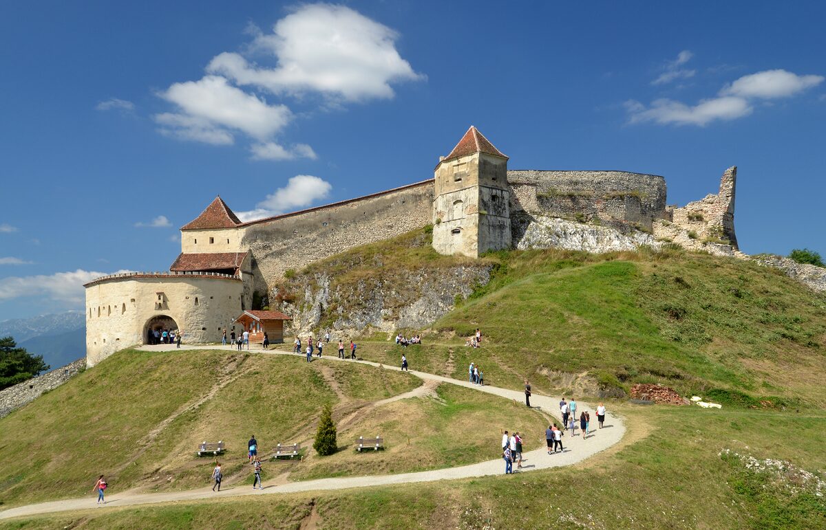 Râșnov Fortress with its walls and square towers on a grassy hill, with a winding path leading up to it