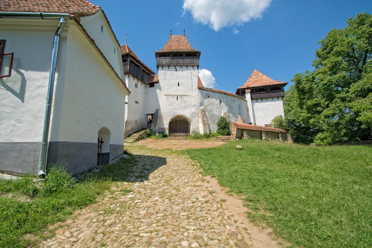 A cobbled path leading to the white walls and towers of the fortified church in Viscri