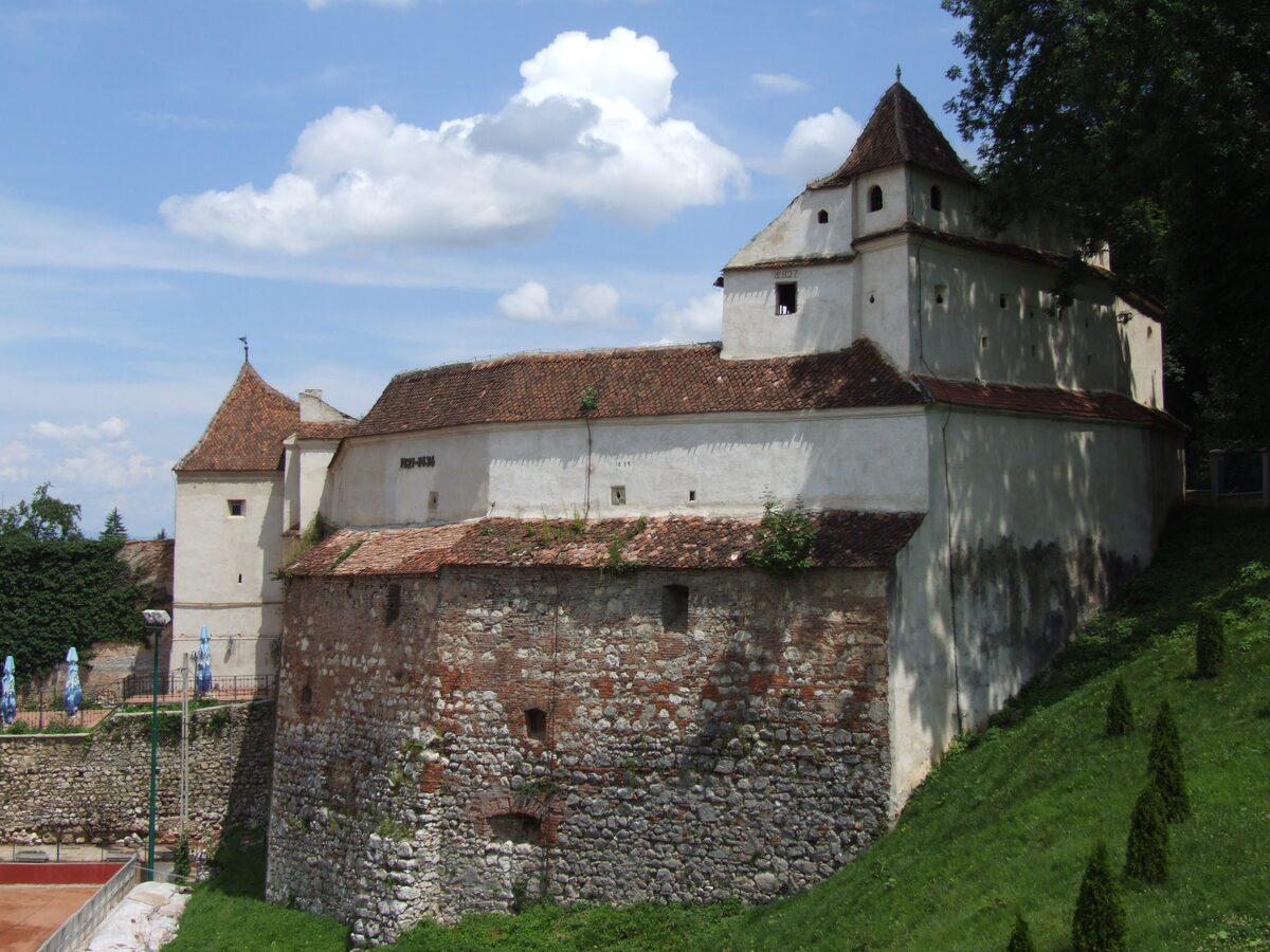 The Weavers' Bastion in Brașov, a stone bastion with a whitewashed upper part and red tile roofs on a green slope