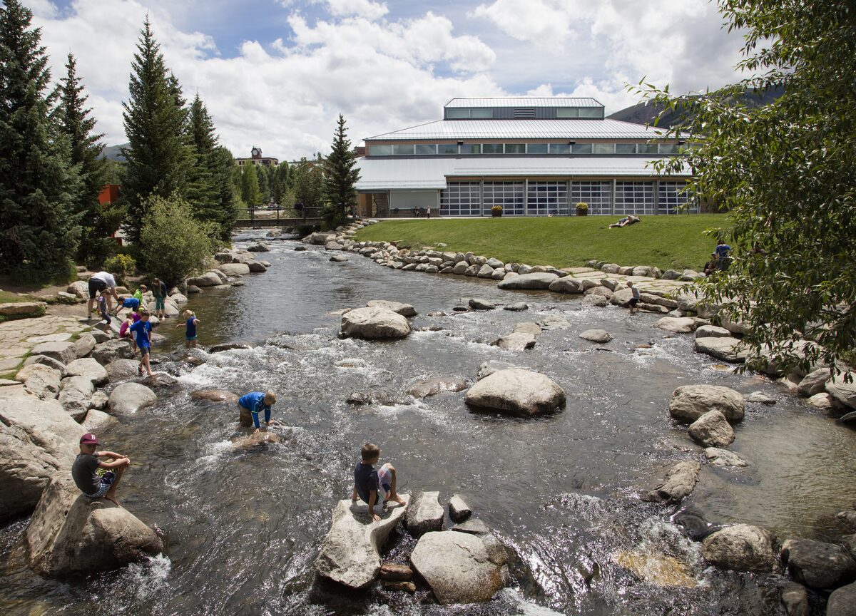 The Blue River tumbling over rocks through Breckenridge's Riverwalk, with the Welcome Center building behind the trees