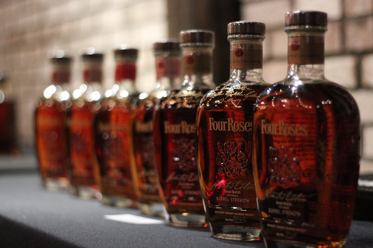 A row of amber bourbon bottles lined up on a bar, with the nearest ones sharp in the foreground