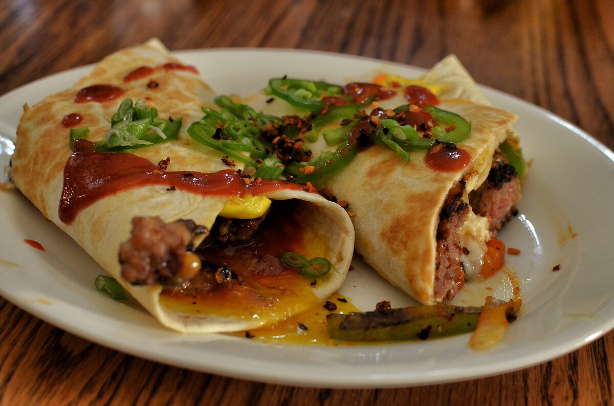 Two breakfast burritos cut open on a plate, filled with meat and egg and topped with red sauce and green onion