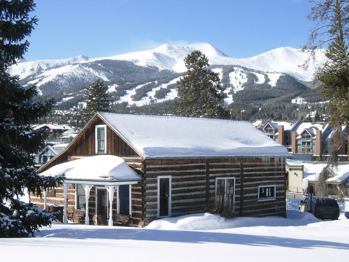The Edwin Carter Museum, a log building under a roof of snow, with the ski runs of Peak 8 rising behind the town