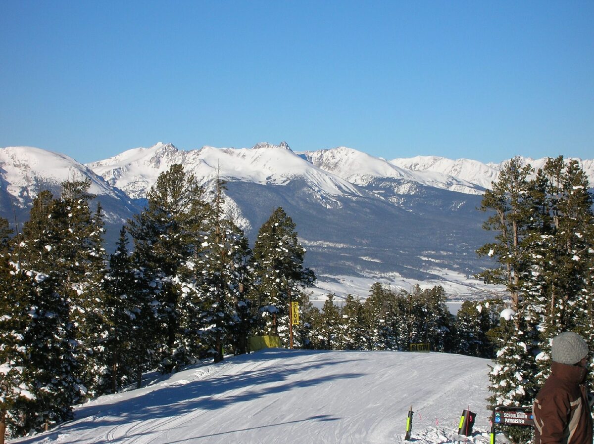 A groomed run at the top of Keystone with snowy pines and the Tenmile Range stretching away under a blue sky
