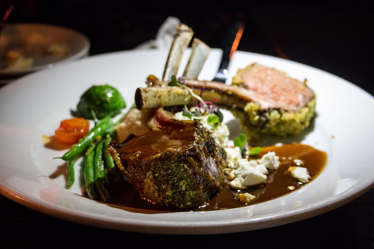 A herb-crusted rack of lamb with mashed potatoes, green vegetables and rosemary jus on a white plate