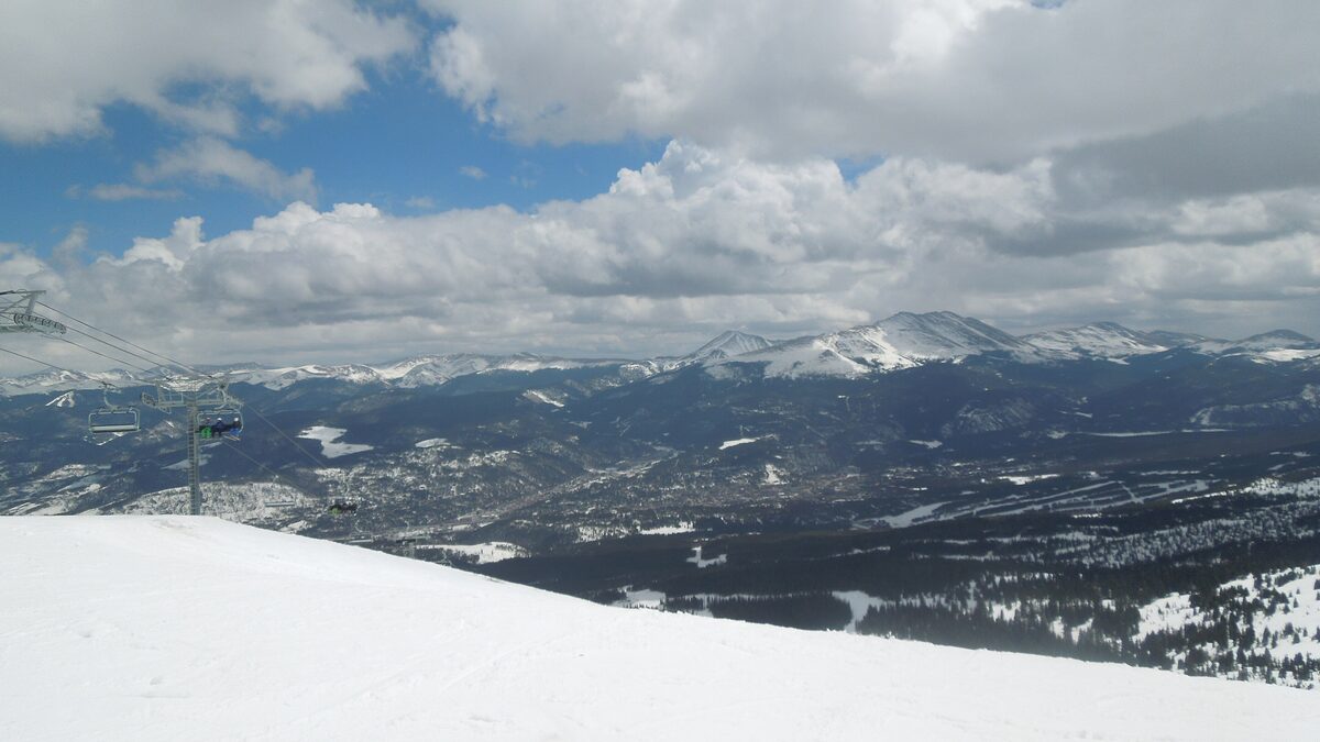 Breckenridge and the Blue River valley seen from the snowy top of Peak 6, with a lift line on the left and distant ranges beyond