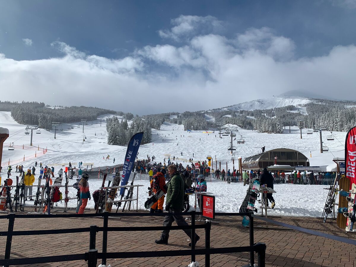 The busy Peak 8 base area in winter, with ski racks, lift queues and the snowy slope of Peak 8 behind