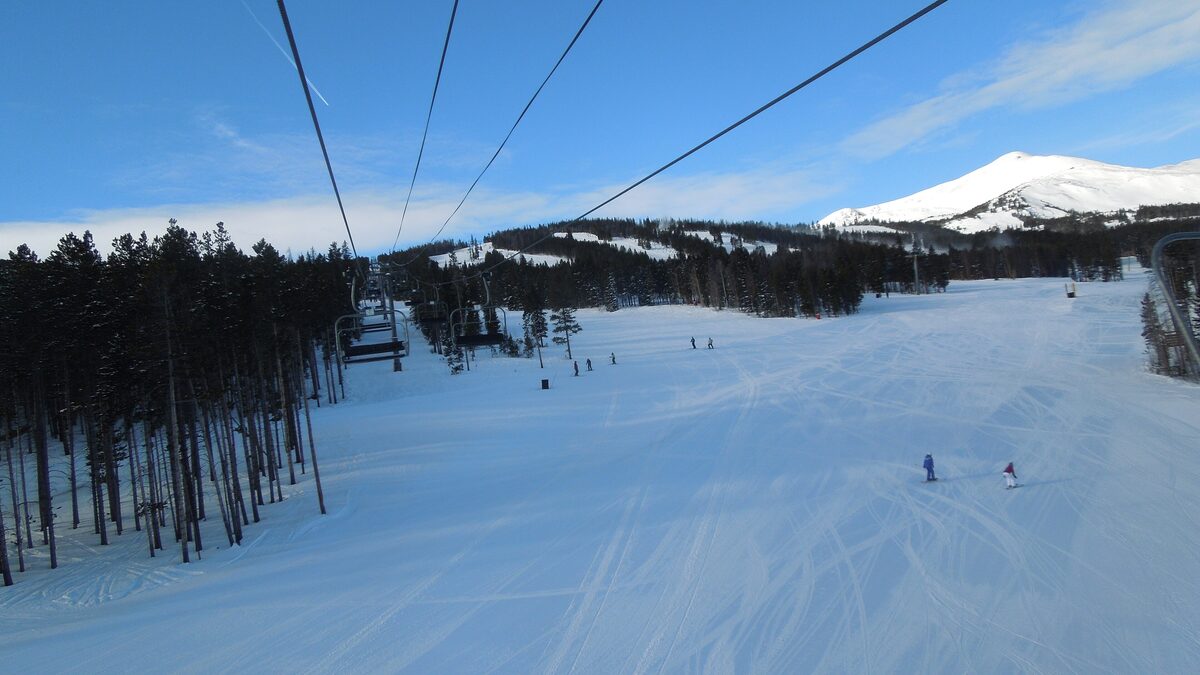 A wide groomed run on Peak 9 with a chairlift line beside it and the snowy top of Peak 8 in the distance